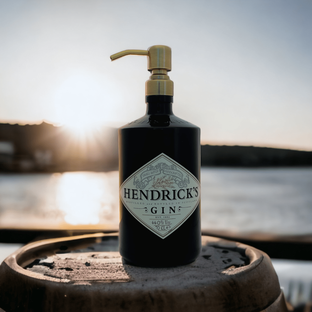 Hendrick's gin soap dispenser with vintage gold finish positioned on top of an oak wine barrel in front of the sea