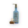 Turquoise bombay sapphire gin soap dispenser with vintage gold pump that is stood behind an empty shot glass and a champagne cork. White backgrounf