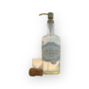 Santisma Trinidad soap dispenser with a vintage bronze pump. The bottle is empty on a white background placed next to an empty shot glass and champagne cork